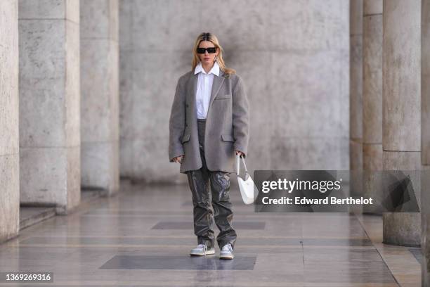 Natalia Verza wears black sunglasses, a silver and black pendant earring from Prada, a white shirt from Karl Lagerfeld, a gray oversized felt /...