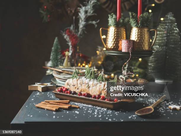 traditional german christmas stollen cake on long plate with cranberries, tree shapes rosemary, cinnamon sticks, festive christmas decoration and powdered sugar at grey kitchen table with dark wall background - cake table photos et images de collection