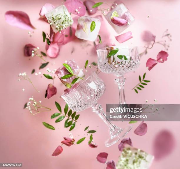 flying crystal champagne glasses with floral ice cubes with rose petals and green leaves at blurred pale purple background - crystal glasses stockfoto's en -beelden
