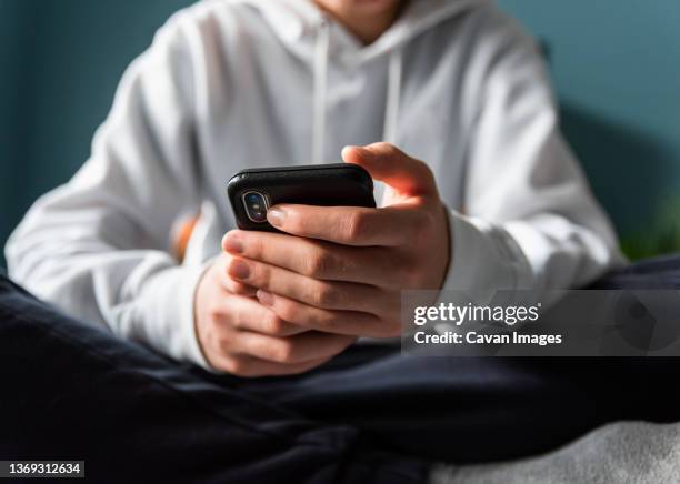 close up of hands of teen boy in white sweater texting on phone. - topnews foto e immagini stock