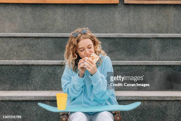 young woman bite street food outdoors and drinking coffee. - shawarma stock-fotos und bilder