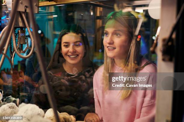 two girls play in a claw machine to get soft toys - mechanical claw stock-fotos und bilder