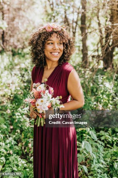 woman standing in woods with fresh flowers and floral crown - bruidsmeisje stockfoto's en -beelden