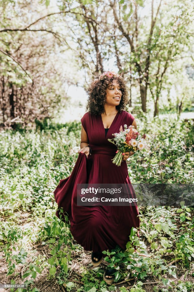 Black woman walks through wooded area holding bouquet