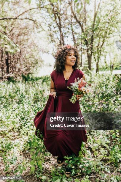 black woman walks through wooded area holding bouquet - blumenkrone stock-fotos und bilder