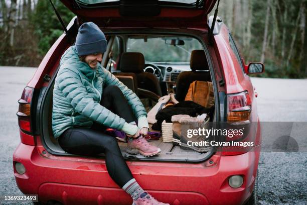 young woman changes into trail running shoes in the back of her car - strumpbyxor bildbanksfoton och bilder