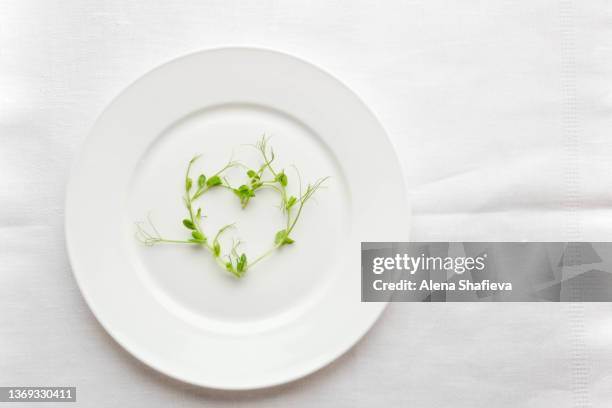 microgreen pea sprouts laid out in a heart shape on a white plate. - rucola foto e immagini stock