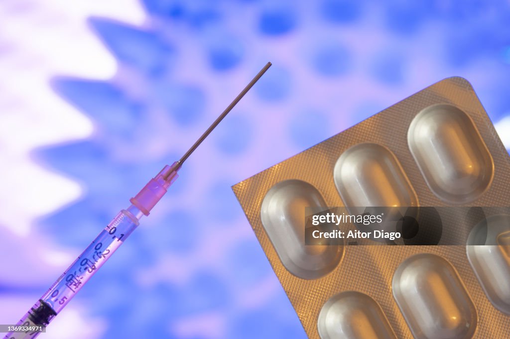 Pills and a Syringe with vaccine  against Covid-19 for different COVID-19  mutations as Omicron or Delta. A coronavirus in the background.