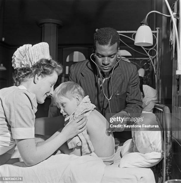 Doctor examines the back of a young patient with a stethoscope as a nurse helps him holding his shirt up at a London hospital, UK, 1948.