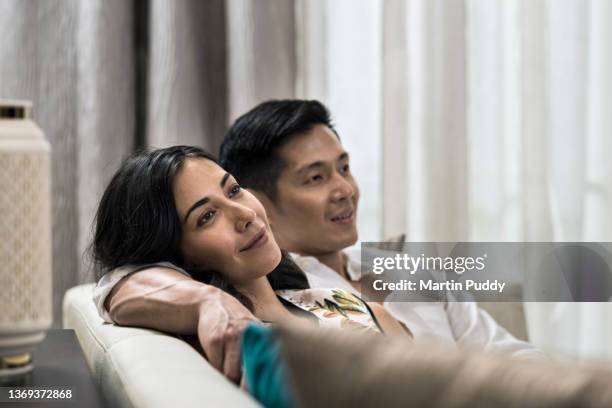 young multiracial couple at home, sitting on sofa in living room - daily life in indonesia stock pictures, royalty-free photos & images