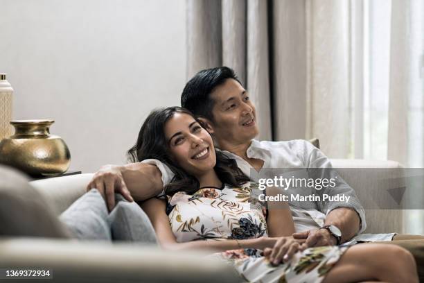 young multiracial couple at home, sitting on sofa in living room - chinese indonesians stock pictures, royalty-free photos & images