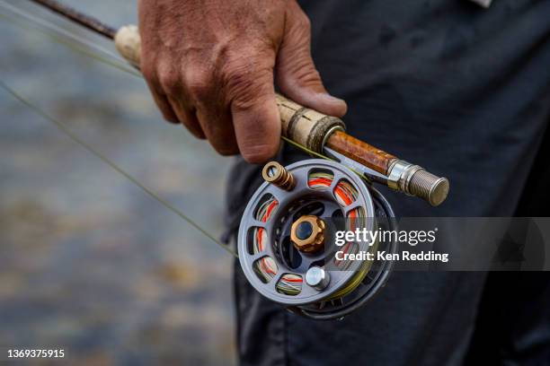 fly fishermans hand holding rod and reel - fishing reel stock pictures, royalty-free photos & images
