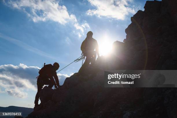 rock climber assisting another - team climbing up to mountain top stockfoto's en -beelden