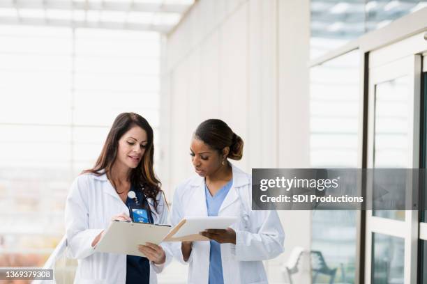 female healthcare professionals meet to discuss patient records - laboratoriumjas stockfoto's en -beelden