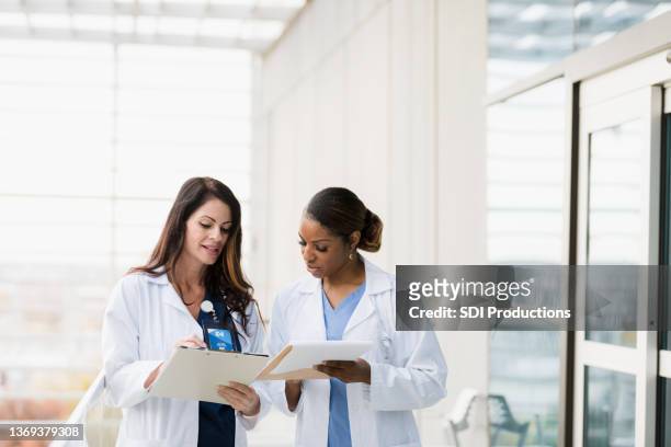 female healthcare professionals meet to discuss patient records - doctor white lab coat stock pictures, royalty-free photos & images
