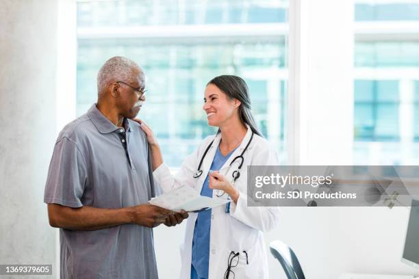 doktor lächelt und versucht, traurigen älteren mann zu ermutigen - heilbehandlung stock-fotos und bilder