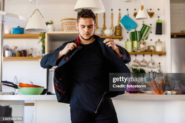 junger männlicher koch, der seine uniform anzieht, bevor er essen zubereitet - get dressed male stock-fotos und bilder