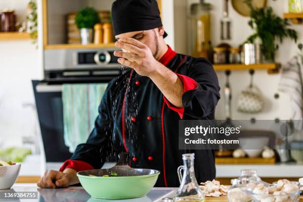 professional chef sprinkling a pinch of salt into a pan - adicionar sal imagens e fotografias de stock