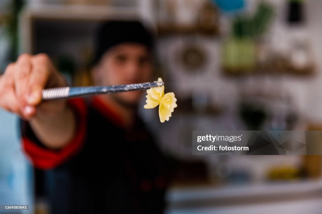 Selective focus shot of chef holding a bowtie pasta in kitchen tweezers