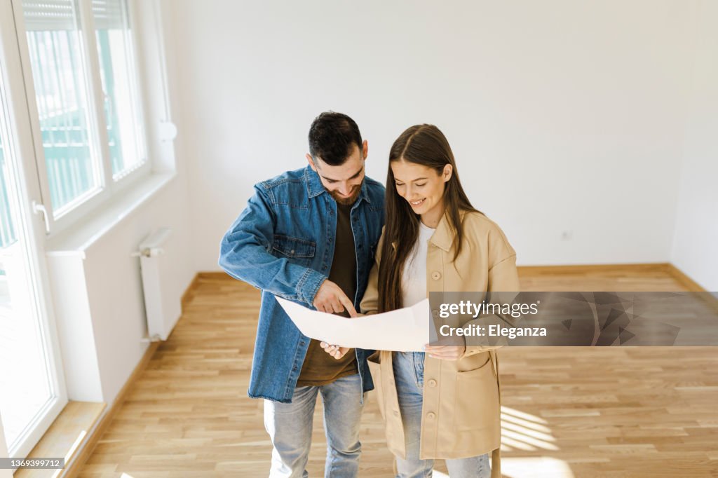 Happy family couple discussing interior design of new apartment, Man Talking With Woman In Empty Room Of New House