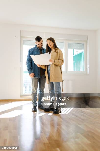 happy family couple discussing interior design of new apartment, man talking with woman in empty room of new house - new flat stock pictures, royalty-free photos & images