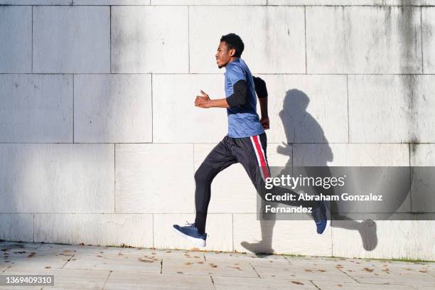 young african-american man running and jumping on sidewalk against concrete wall - running midair stock pictures, royalty-free photos & images