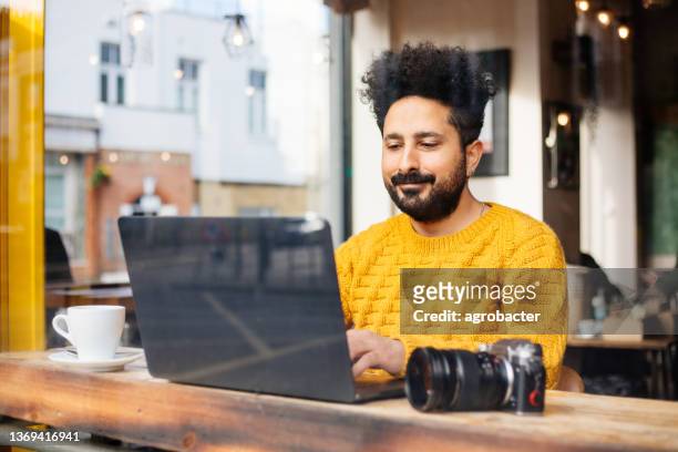 photographer drinking coffee and using laptop at cafe - yellow shirt stock pictures, royalty-free photos & images