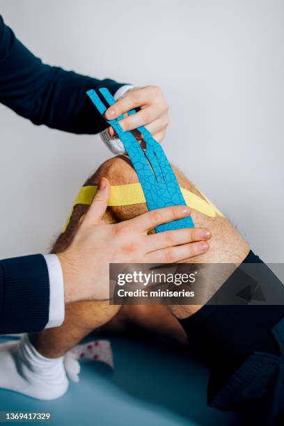 anonymous physical therapist applying kinesio tape to the patient's knee - kinesiotape stock pictures, royalty-free photos & images