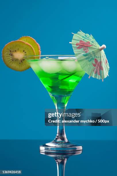 tropical green cocktail,close-up of drink in glass against blue background - cocktail umbrella stock pictures, royalty-free photos & images