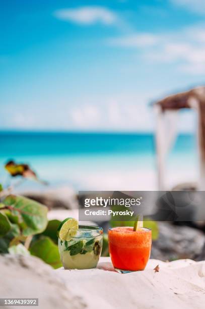 close-up of two cocktails on the sand, with a turquoise sea in the background - caribbean dream stock pictures, royalty-free photos & images