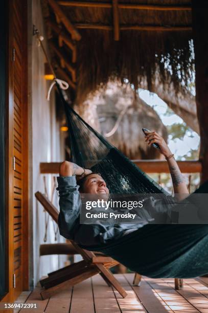 ein junger, gutaussehender mann in einer hängematte macht einen videoanruf mit einem smartphone - schaukel mann stock-fotos und bilder
