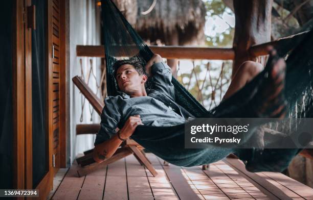 a handsome young man relaxing in a hammock - grass hut stock pictures, royalty-free photos & images