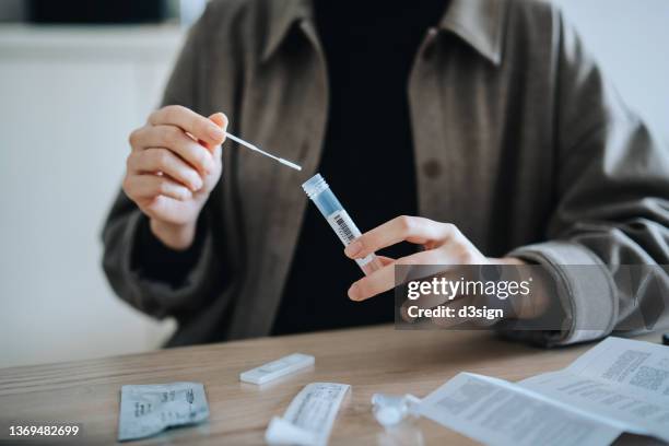 cropped shot, mid-section of young asian woman carrying out a covid-19 rapid lateral flow test, dropping cotton swab in a protective plastic tube with liquid after nasal swab test for a rapid self test at home - cotton swab stock pictures, royalty-free photos & images