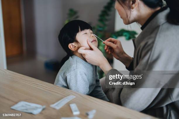 young asian mother carrying out a covid-19 rapid lateral flow test to her daughter, putting a nasal swab into her daughter's nose for a coronavirus rapid self test at home - antibody testing stock-fotos und bilder