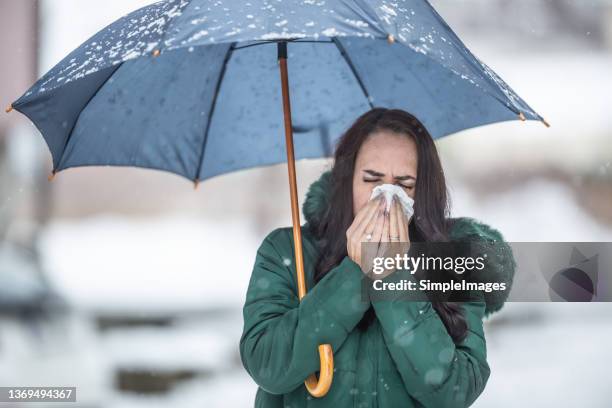 woman holding umbrella on the cold snowy day sneezes into a hankerchief. - catarro fotografías e imágenes de stock