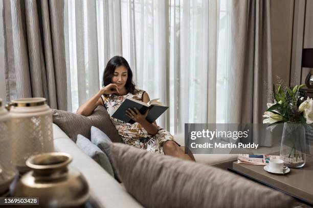young attractive woman working from home, reading a notebook while sitting on sofa in living room - newspaper luxury bildbanksfoton och bilder