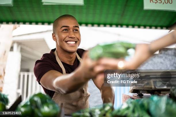 seller handing a vegetable to a customer at a street market - sälja bildbanksfoton och bilder
