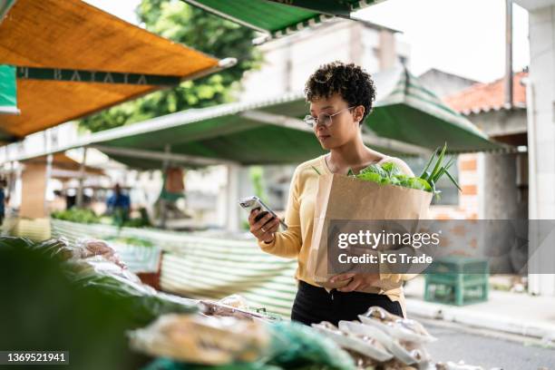 junge frau mit dem handy auf einem straßenmarkt - landwirtschaftsmesse stock-fotos und bilder