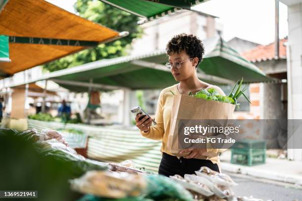 young woman using the mobile phone at a street market - homegrown produce 個照片及圖片檔