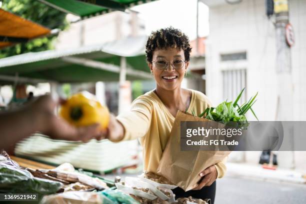 portrait d’une jeune femme achetant un vendeur de poivrons sur un marché de rue - marché de plein air photos et images de collection