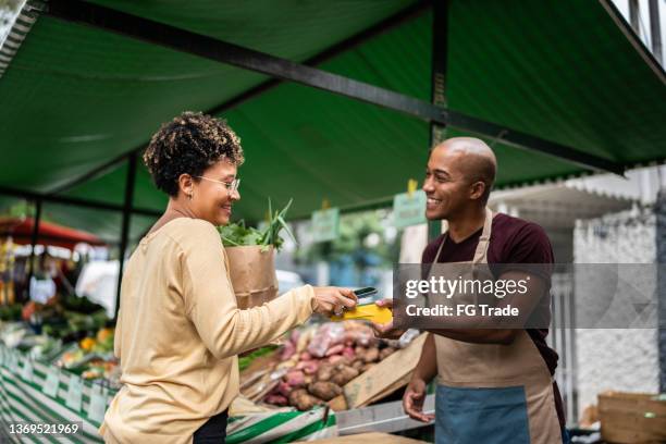 joven pagando con teléfono móvil en un mercadillo - mercado de productos de granja fotografías e imágenes de stock