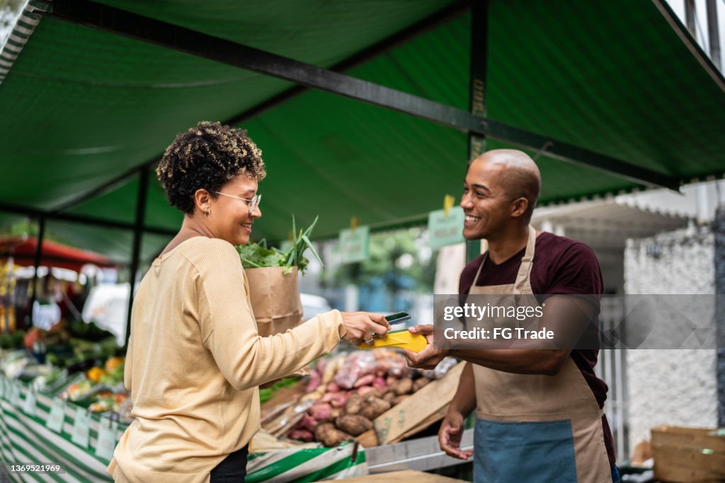 Young woman paying with mobile phone at a street market