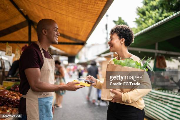 giovane donna che paga con il cellulare in un mercato di strada - paying supermarket foto e immagini stock
