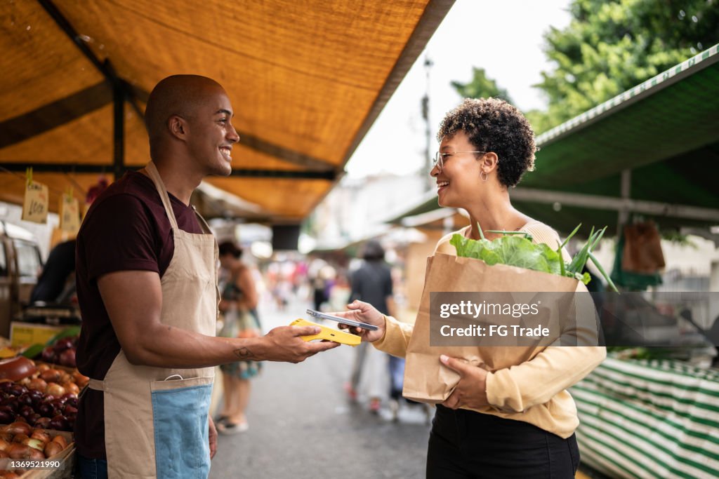Young woman paying with mobile phone at a street market