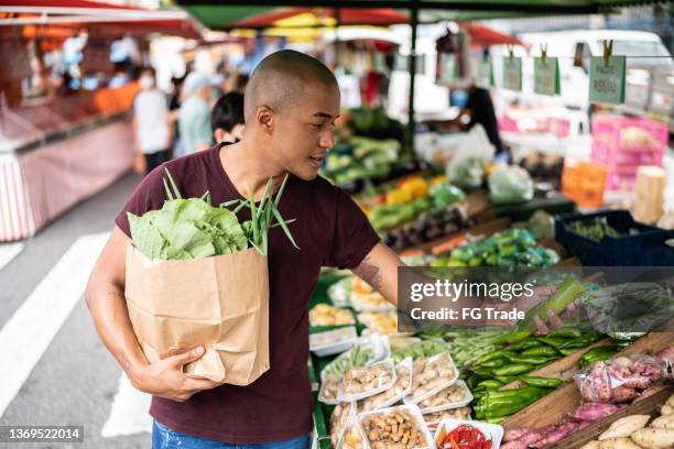 giovane che sceglie il cetriolo in un mercato di strada - mercato di prodotti agricoli foto e immagini stock