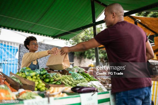 seller handing the shopping bag to a customer at a street market - farmer's market imagens e fotografias de stock
