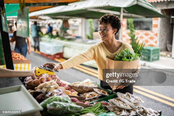 une jeune femme payant avec son téléphone portable sur un marché de rue - marché de plein air photos et images de collection