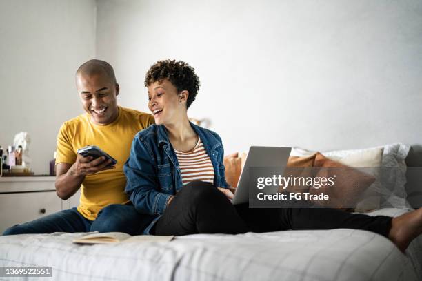 ehemann zeigt seiner frau zu hause etwas auf dem handy - couple looking laptop stock-fotos und bilder