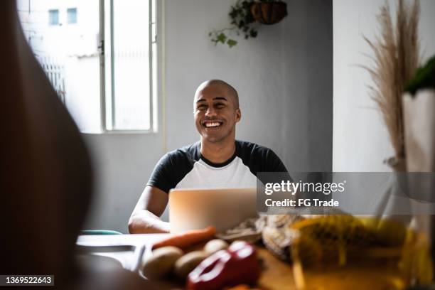 young man using the laptop and talking to his wife at home - freelance work candid stock pictures, royalty-free photos & images