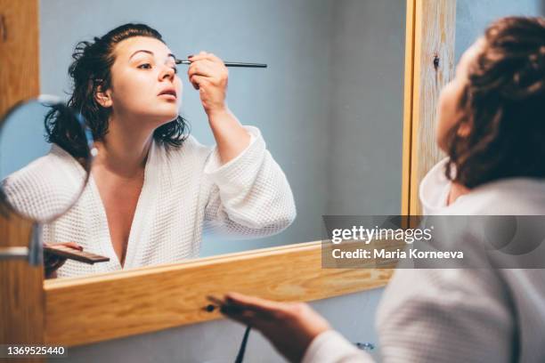 young woman after shower wearing white bathrobe and doing make up. - ladies day stock pictures, royalty-free photos & images